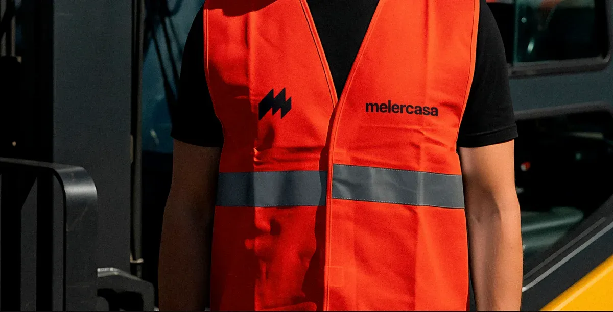 Chaleco reflectante naranja con el símbolo de Melercasa en el pecho y el nombre al otro lado.